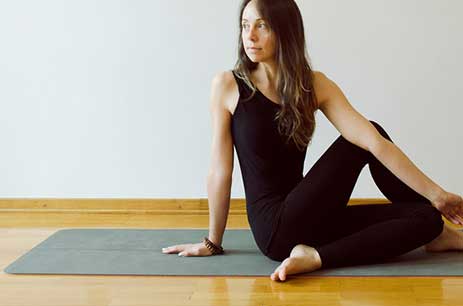 A woman in black workout attire sitting on a yoga mat indoors.